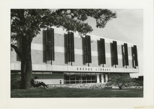 Exterior of Kresge Library with a student sitting underneath a t